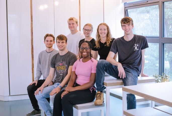 Image: 7 of the interns at Crux Product Design, sat on a table in the office with a white background